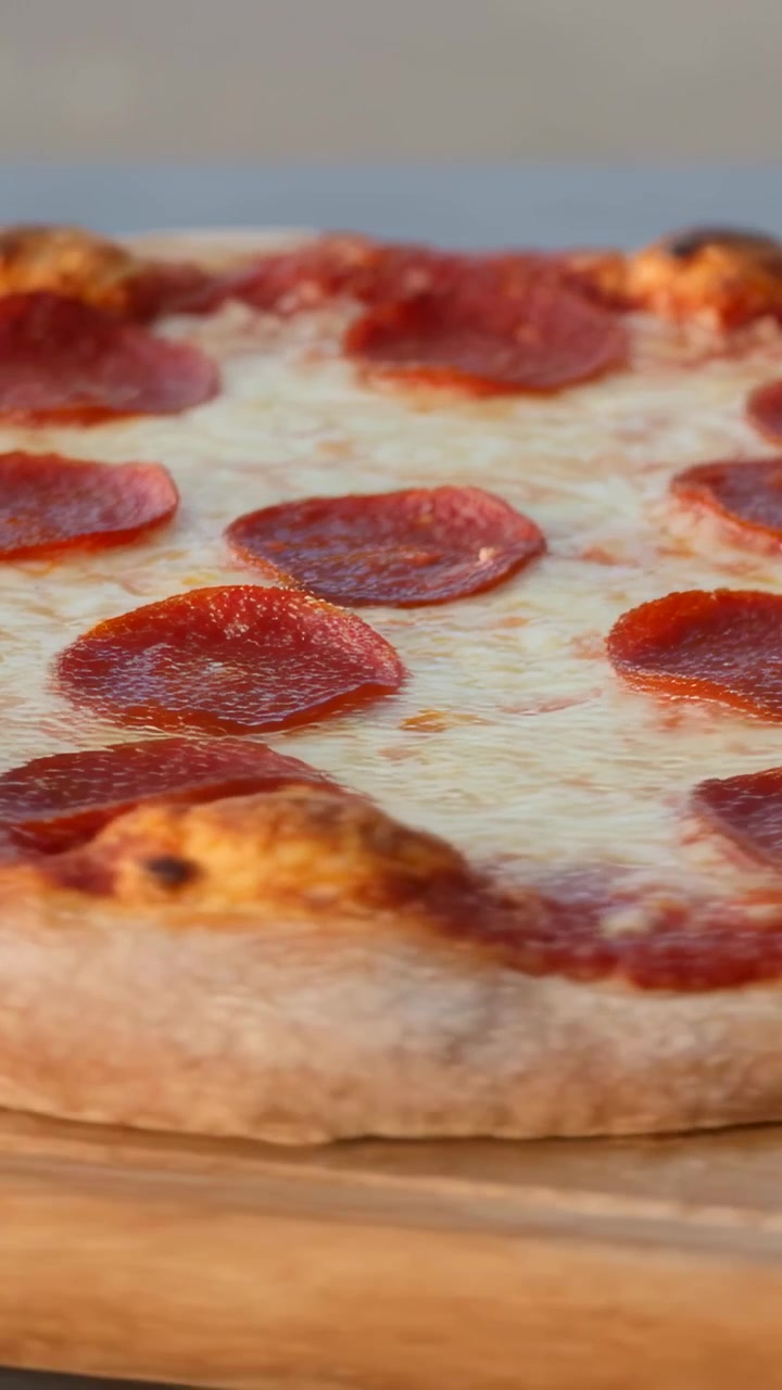 Video verticale: La telecamera panoramica rivela una pizza ai peperoni su un tagliere, mettendo in risalto i condimenti e il bordo.
