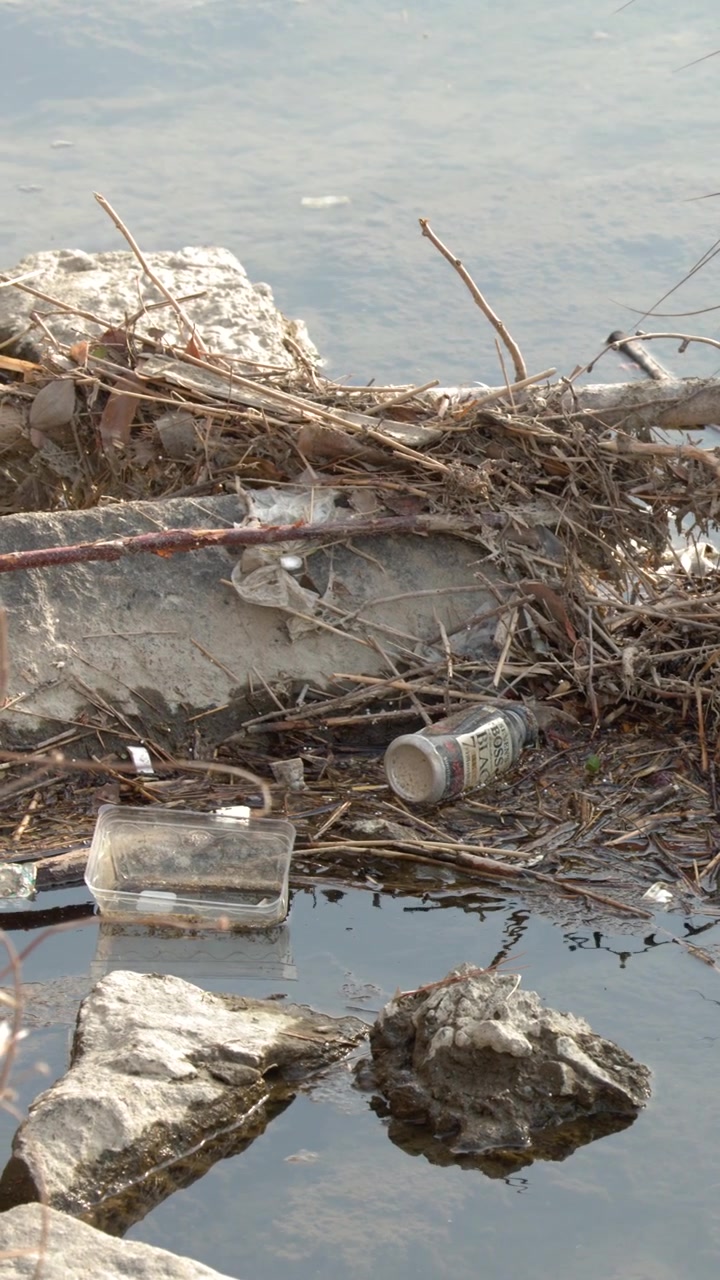 Residuos plásticos y escombros contaminando la orilla de un río