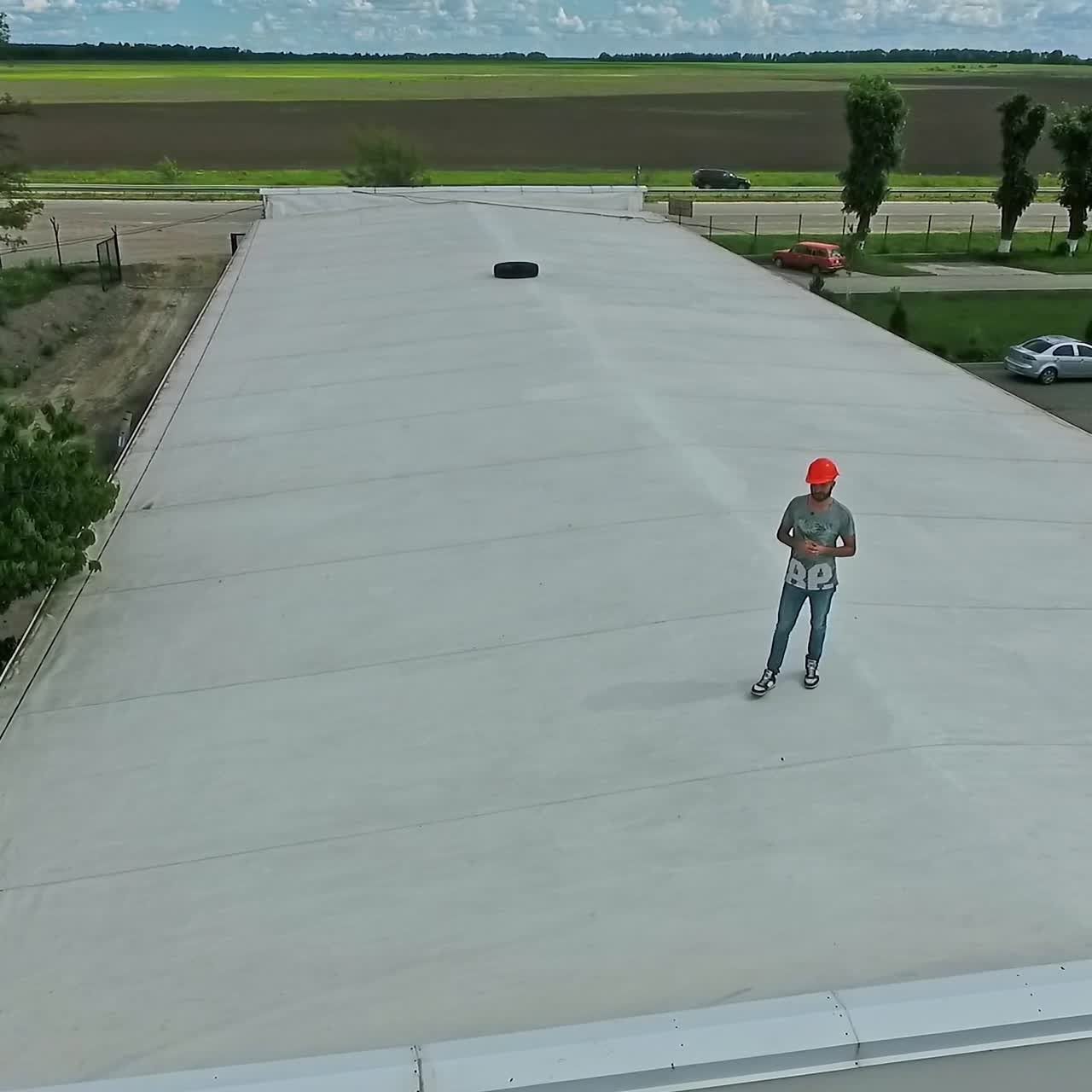 Worker on a flat roof of the industrial building. Man in safety helmet stands on roof and looking at camera. Aerial view.