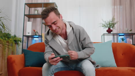 Worried-funny-young-man-boy-playing-shooter-online-video-games-celebrate-win-on-smartphone-at-home