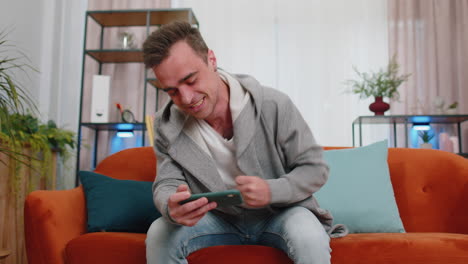 worried funny young man boy playing shooter online video games celebrate win on smartphone at home