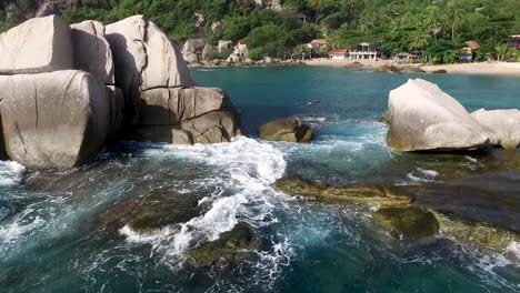 Waves-hitting-rocks-steady-shot-sandy-beach-palm-tree-background