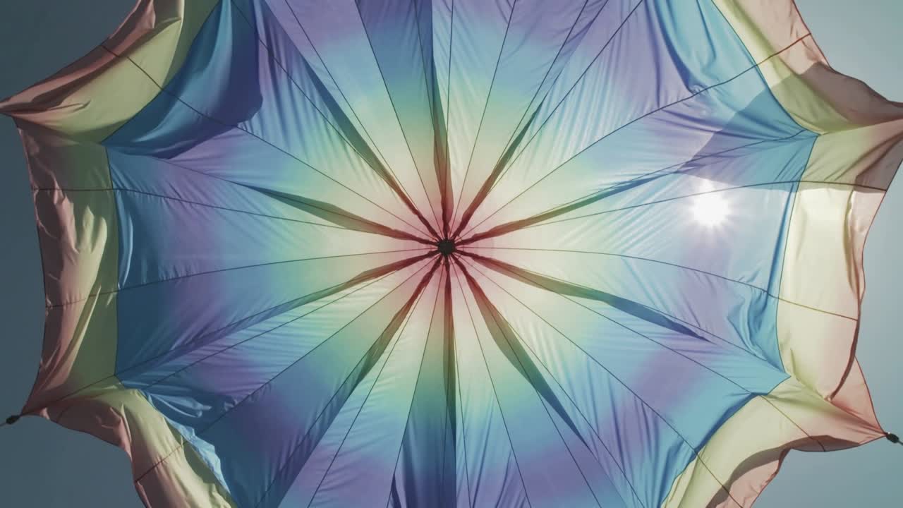 Brezza che si alza, la cupola colorata dell'ombrellone che ondeggia, le stecche che si muovono e ruotano mentre il riflesso del sole scivola.
