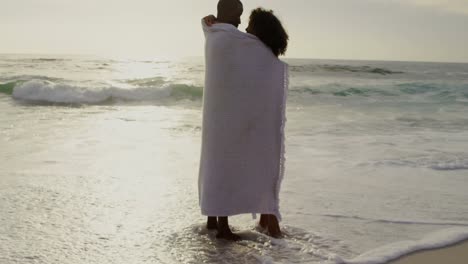 side view of african american couple wrapped in blanket on the beach 4k