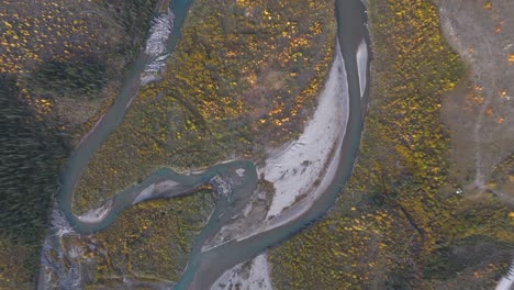 birds eye view of a beautiful meandering river amongst the vibrant fall colours of deciduous tress and a small camp along the riverbank