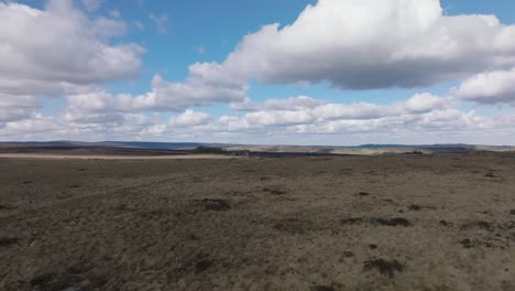 aerial drone footage descending over rural, open plains and moorland with a cloudy, blue sky and beautiful rolling hills