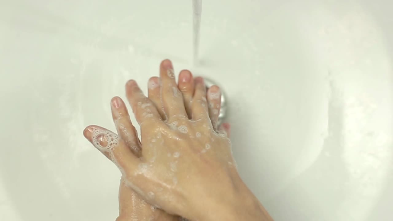 Primo piano di una persona che si lava le mani con acqua e sapone in un lavandino bianco