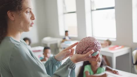 video of happy caucasian female teacher holding brain model in class of diverse pupils