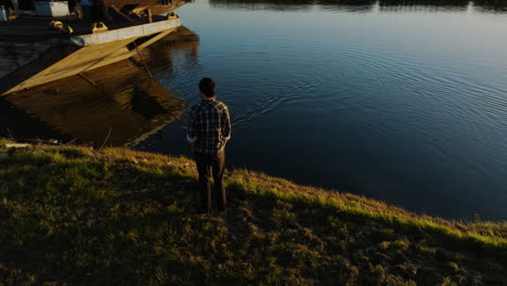 órbita aérea alrededor del hombre esperando en el borde de las aguas del canal como perro nada de vuelta a la orilla del río