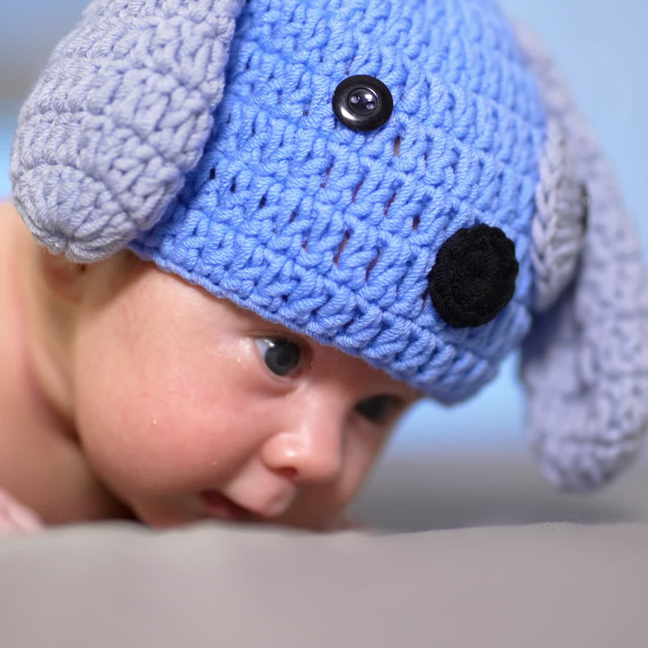 Puppy cap on a baby head. Lovely child lying on the belly and trying to keep his head up. Toddler in a funny hat with ears close up