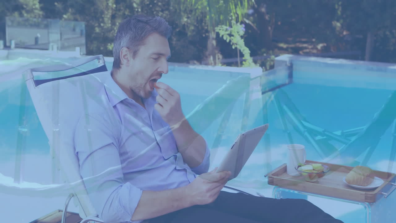 Relaxing by pool, man reading newspaper with breakfast tray beside him
