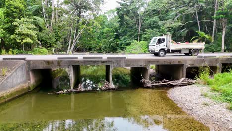 aerial view of a truck crossing a bridge over a rainforest stream in port douglas, australia. lush greenery surrounds the scene