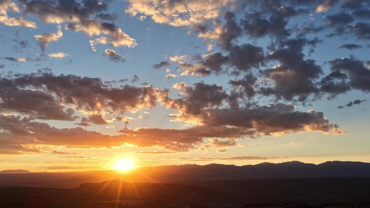 Timelapse de dron 4K UHD capturando un impresionante amanecer en el alto desierto. Un brillante estallido solar corona la oscura cresta de la montaña, iluminando nubes de rápido movimiento con tonos dorados y naranjas radiantes