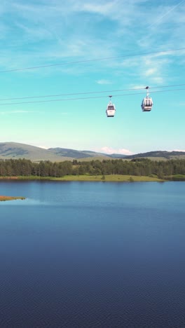 vertical drone shot of gold gondola lift cabins above blue lake and green landscape