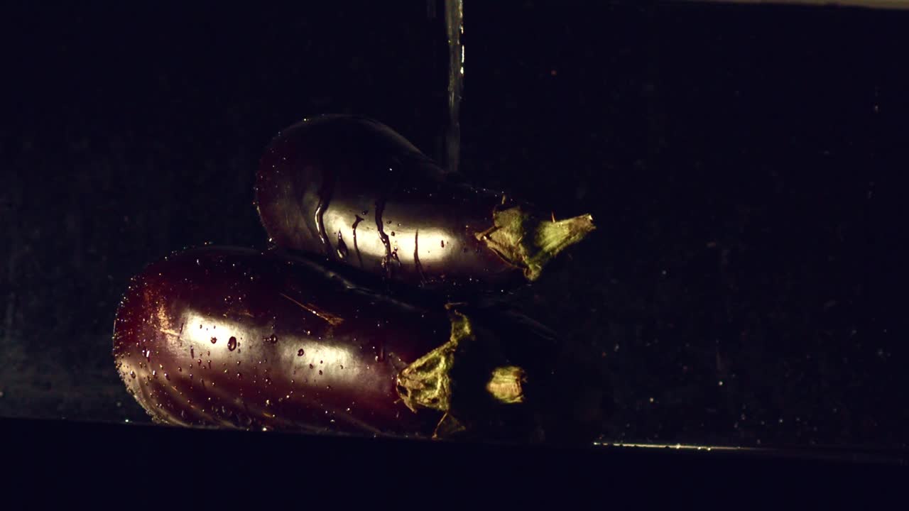 verter agua sobre dos berenjenas contra un fondo oscuro - cerrar