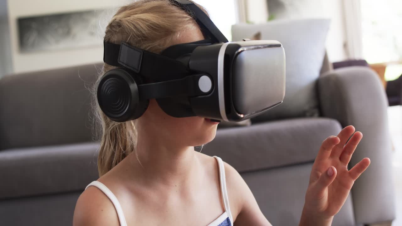 Female child moving from stillness, reaching VR headset with headphones, exploring scene on sofa