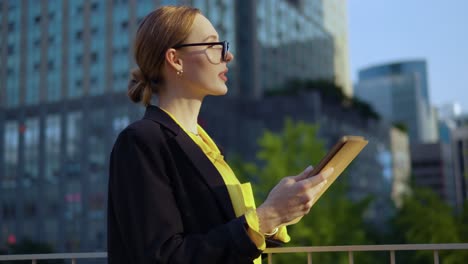 Businesswoman-in-eyeglasses-using-iPad-tablet-outside-standing