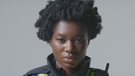 studio portrait of serious young female police officer against plain background