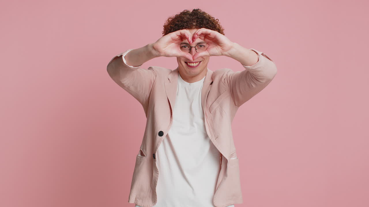 un joven sonriente hace un gesto de corazón demuestra un signo de amor expresa buenos sentimientos y simpatía