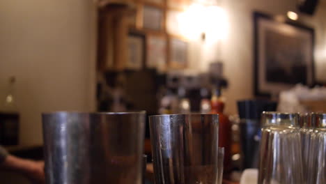 bartender pours three liquors from bottle into tin cocktail shakers