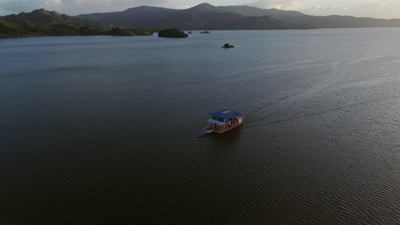 Ferry boat with tourist on water reserve of Hatillo Dam at sunset time. Aerial orbit shot. Beautiful landscape in Dominican Republic. Wide shot.