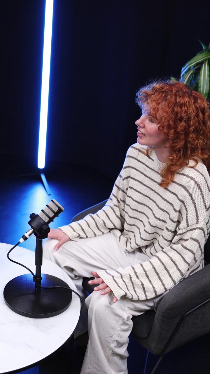 Giovane donna dai capelli rossi che ascolta un'intervista in uno studio moderno