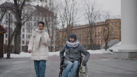 Muslim-Woman-And-Her-Disabled-Friend-In-Wheelchair-Taking-A-Walk-In-City-In-Winter-1