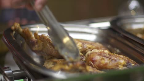 muslos de pollo cocidos dispuestos en una sartén de acero inoxidable usando pinzas, filmados de cerca