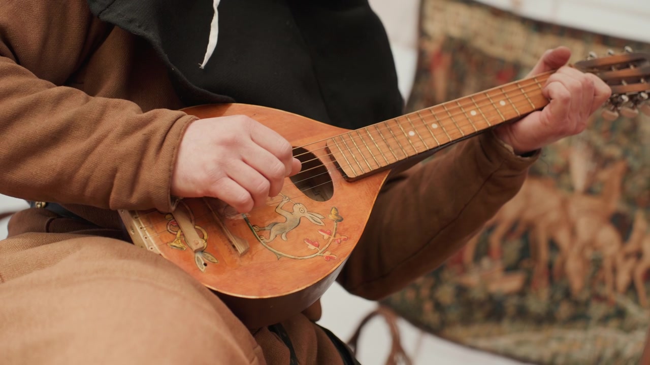 Persona tocando un instrumento de cuerda en un entorno interior con tela estampada de fondo, con detalles en marrón y negro.