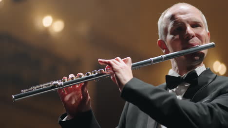 flautista de cabello gris está tocando música en el salón filarmónico ensayo o concierto de orquesta sinfónica