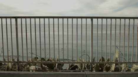 Surfers-on-the-Pacific-Ocean,-as-viewed-through-a-guard-rail-at-a-vista-in-Encinitas,-California