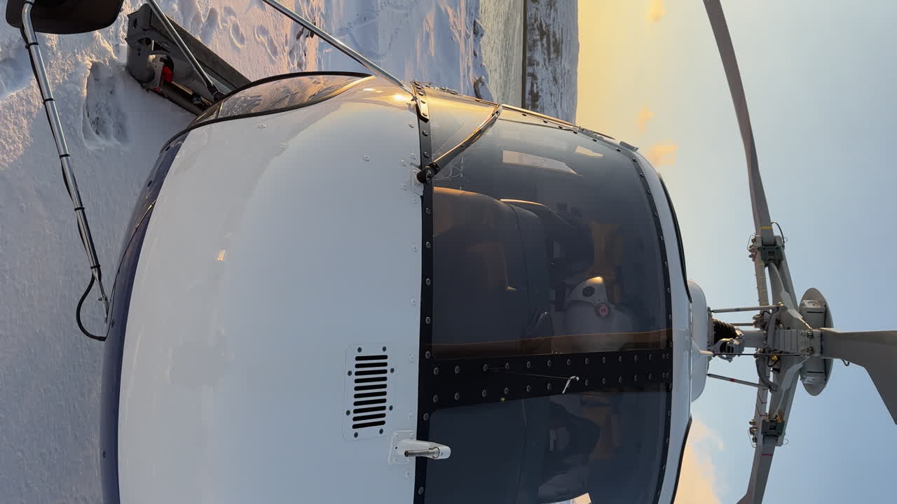 Close up panning shot of a helicopter parked in the snow near the ocean on an arctic island with wind turbines in the distance, vertical