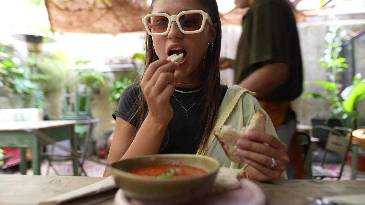 Young Woman Eating Tomato Soup and Bread in Outdoor Cafe