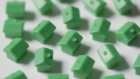 home buying concept with hand clearing away group of green plastic models of houses revolving on white background