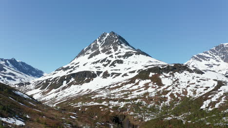 Aerial-view-around-a-snowy-mountain-peak,-on-a-sunny-summer-day,-in-the-Lyngen-alps,-North-Norway---orbit,-drone-shot