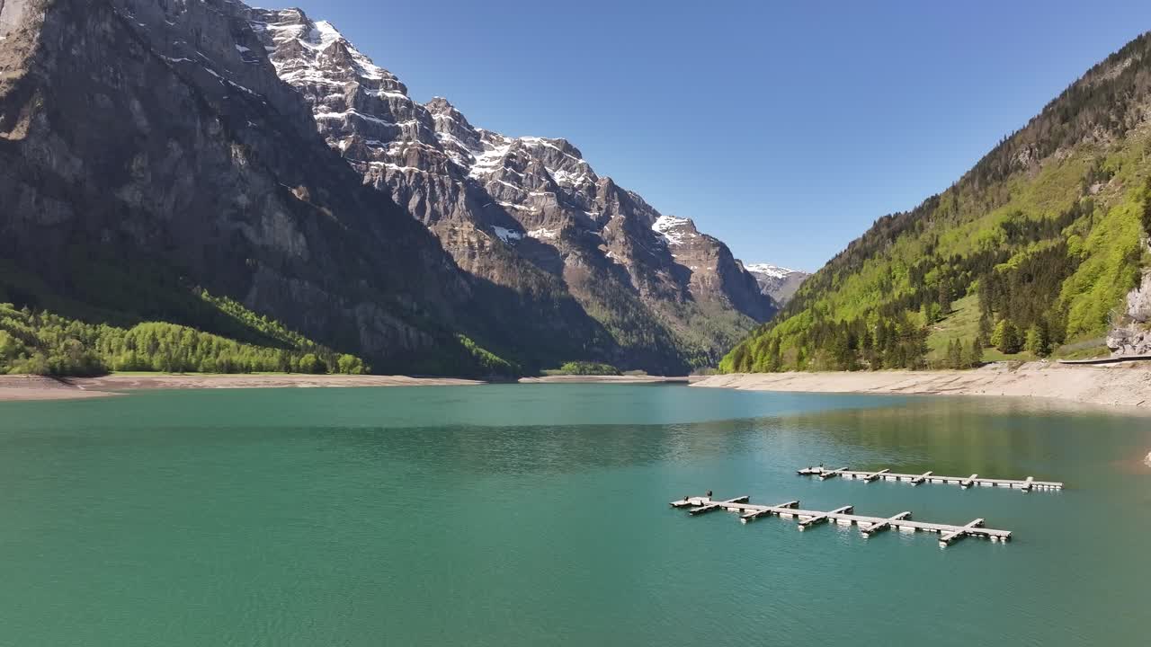 Klöntalersee lake in Glarus, Switzerland, snowy alps, green forest and blue water under clear sky, aerial drone calm view
