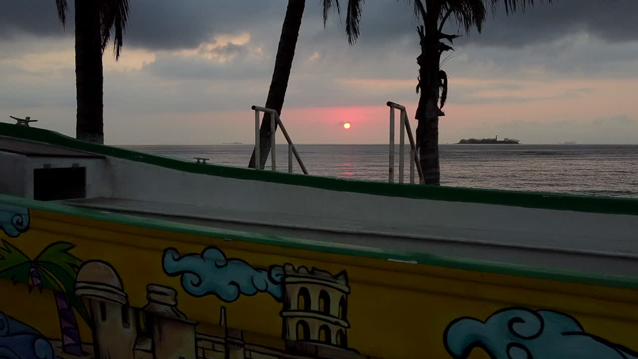 Beautiful sunrise passing through some palmtrees and a boat statue.
