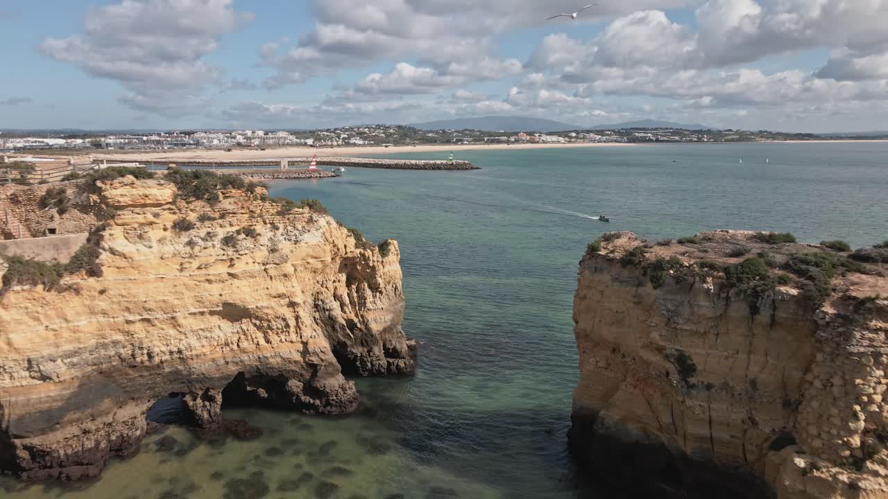 En drone flyr bakover og avslører det dramatiske rommet mellom høye, gylne stabler og klipper omgitt av turkist vann og fjerne strender i Lagos, Algarve, Portugal