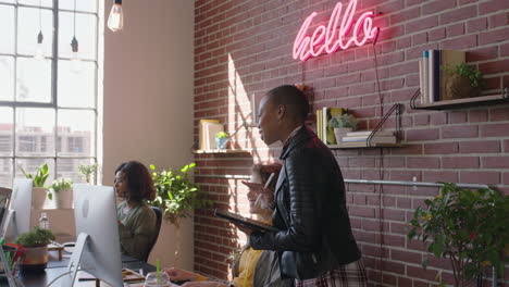 Joven-Mujer-De-Negocios-Afroamericana-Líder-De-Equipo-Disfrutando-De-Una-Carrera-Gerencial-Revisando-A-Sus-Colegas-Que-Trabajan-Usando-Una-Tableta-En-Un-Lugar-De-Trabajo-De-Oficina-Diverso-Caminando-Confiada-Gerente-Femenina