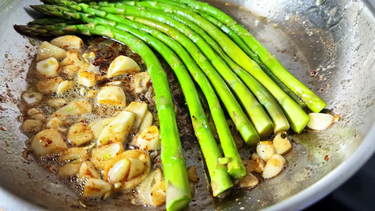 Fresh Asparagus Spears Sizzle in a Pan With Bubbling Butter and Golden Garlic - Close Up