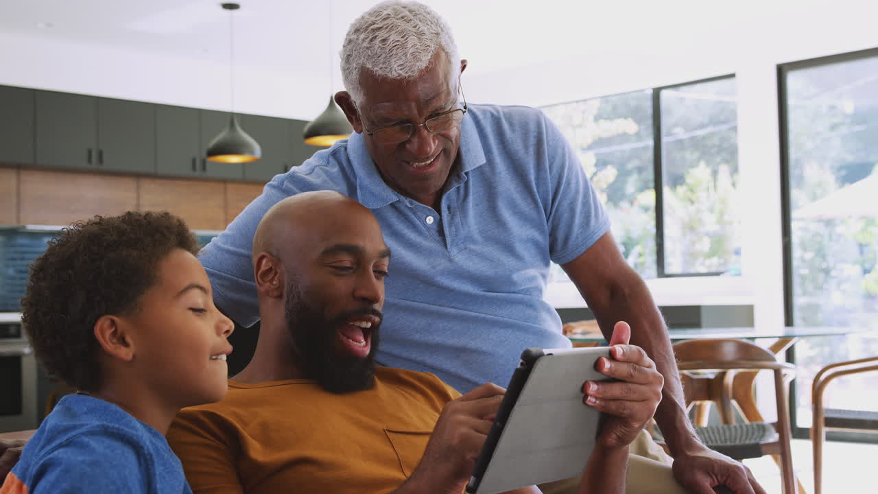 Multi-Generation Male African American Family Sitting On Sofa At Home Using Digital Tablet