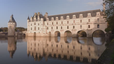 castle of chenonceau reflected in the calm waters of the cher river at golden hour