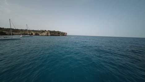 FPV-drone-shot-of-steep-cliffs-and-natural-stone-bridge-along-the-seaside-in-Cala-Varques,-Mallorca,-Spain-during-evening-time