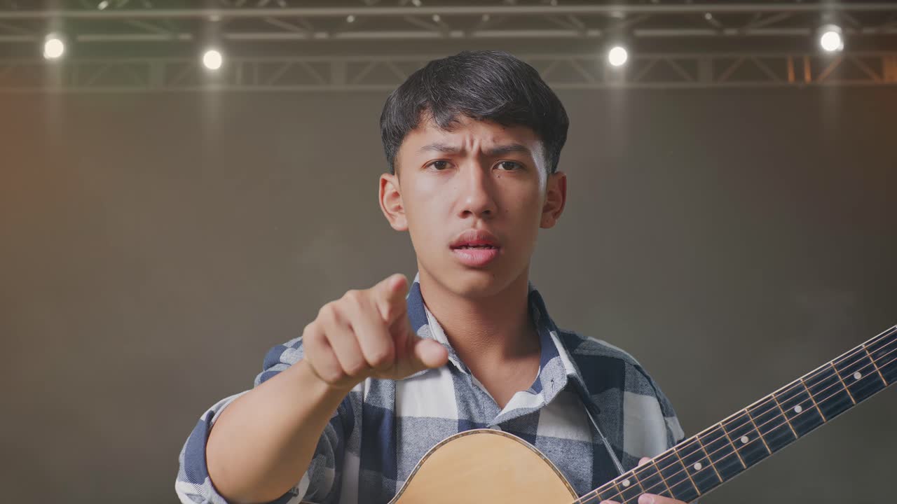 무대 위 에 서 있는 동안 기타 를 들고 카메라 에 소리 지르는 아시아 청소년 의 근접 사진