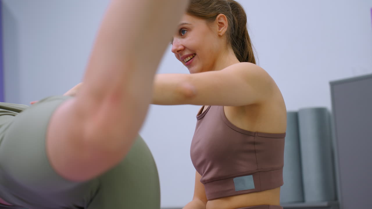 vista enfocada de una mujer en cuclillas con la mano de su instructor en la cintura, sonriendo cálidamente durante una sesión de entrenamiento en un gimnasio bien equipado