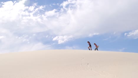 Couple-with-sand-boards-walking-on-the-sand-dune-4k