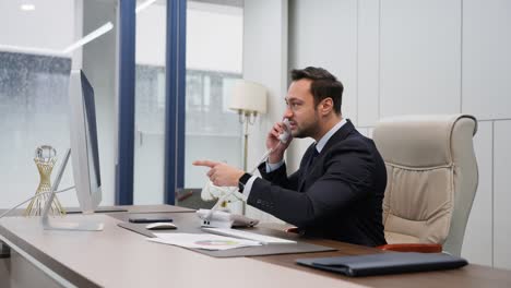 a corporate office setting, an agitated executive in a suit is engaged in a heated phone conversation. seated at desk, he's visibly frustrated, examining documents arguing intensely on a landline