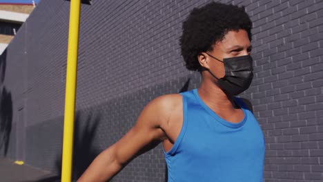 fit african american man exercising in city wearing face mask,stretching in the street