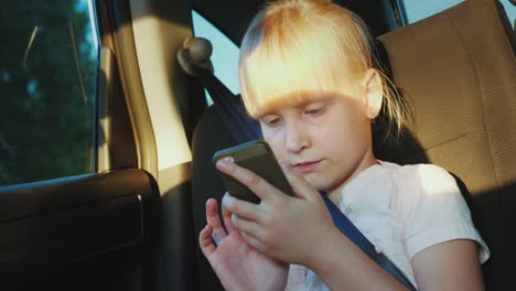 the girl is traveling in a car, playing on a smartphone. on the road with a child