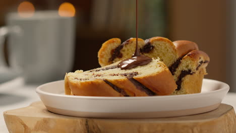 close up of melted chocolate sauce being poured onto chocolate babka bun on plate